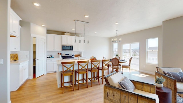 7497 W Sage Slope Way, Herriman, UT 84096 - kitchen with appliances with stainless steel finishes, decorative backsplash, light countertops, light wood finished floors, and a chandelier