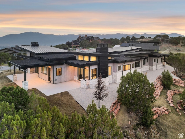 3057 E Corral Peak Cir Unit 147, Heber City, UT 84032 - back of property at dusk featuring a patio, a mountain view, stone siding, a standing seam roof, and driveway