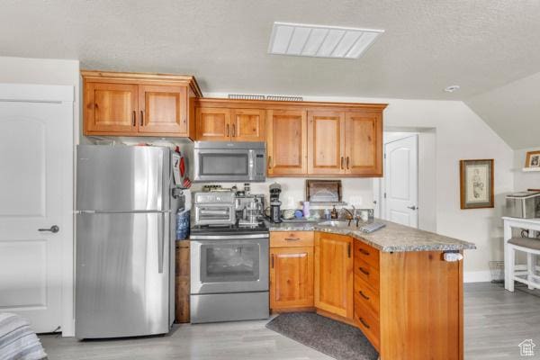 2330 E Meadow Lark Ln, North Logan, UT 84341 - kitchen featuring stainless steel appliances, a peninsula, light wood-style floors, vaulted ceiling, and brown cabinetry