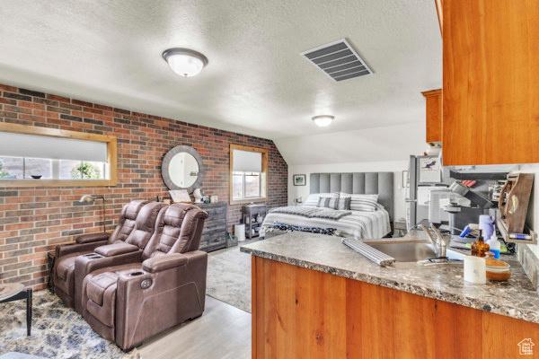 2330 E Meadow Lark Ln, North Logan, UT 84341 - bedroom featuring brick wall, a textured ceiling, lofted ceiling, and light wood-style floors