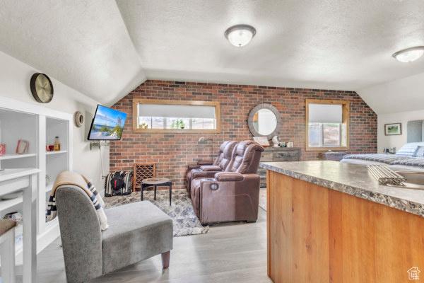2330 E Meadow Lark Ln, North Logan, UT 84341 - living room with brick wall, lofted ceiling, a textured ceiling, healthy amount of natural light, and light wood-style flooring