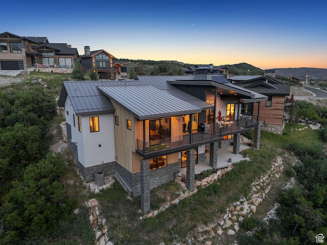 11515 N White Tail Ct, Hideout, UT 84036 - back of house at dusk with a standing seam roof, a balcony, a metal roof, a patio, and stone siding