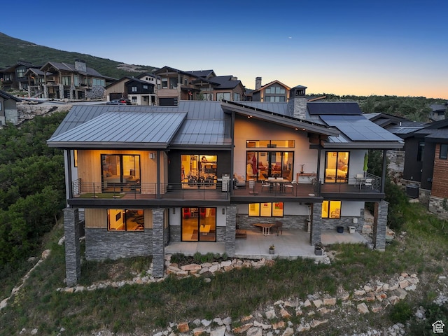 11515 N White Tail Ct, Hideout, UT 84036 - back of property at dusk featuring a standing seam roof, a patio area, stone siding, and a balcony