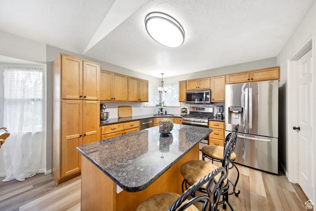5149 W Village Wood Dr, West Valley City, UT 84120 - kitchen with stainless steel appliances, light wood-type flooring, a kitchen breakfast bar, a center island, and a textured ceiling