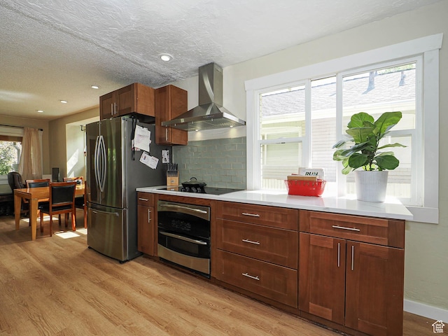 320 E Hollywood Ave S, Salt Lake City, UT 84115 - kitchen featuring wall chimney exhaust hood, stainless steel appliances, light wood-style flooring, light countertops, and a textured ceiling