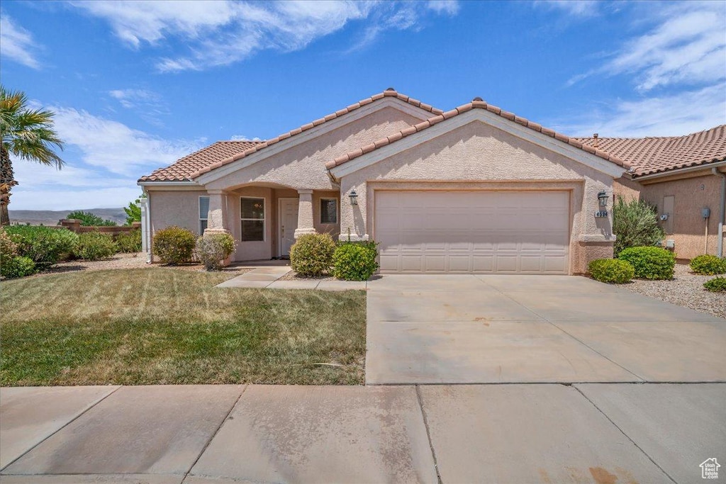 4534 S Big River Dr, St George, UT 84790 - view of front facade featuring an attached garage, a tiled roof, concrete driveway, a front lawn, and stucco siding