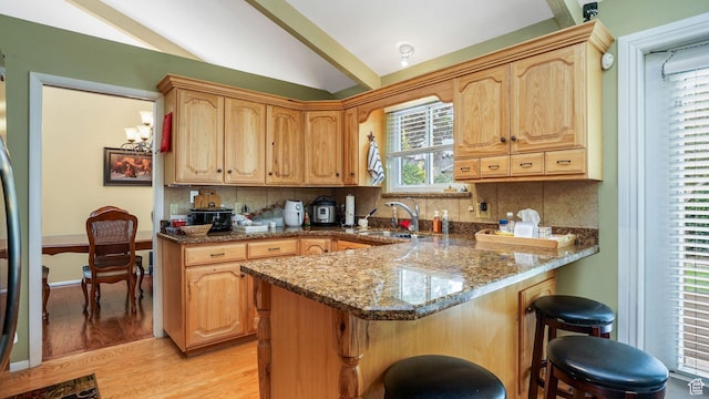 7488 S Blackfriar Cir, West Jordan, UT 84084 - kitchen featuring a kitchen breakfast bar, lofted ceiling, dark stone countertops, light wood finished floors, and a peninsula