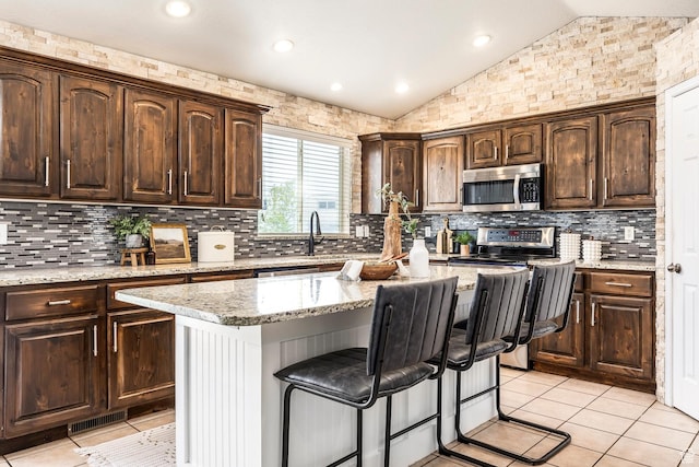 9768 N 5520 W, Highland, UT 84003 - kitchen with appliances with stainless steel finishes, lofted ceiling, a breakfast bar area, dark brown cabinets, and decorative backsplash