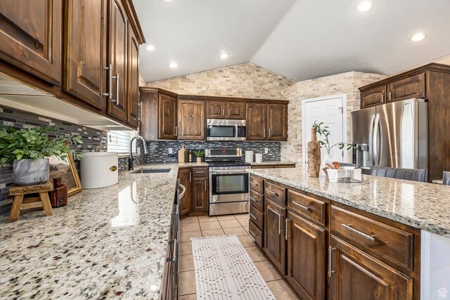 9768 N 5520 W, Highland, UT 84003 - kitchen featuring appliances with stainless steel finishes, vaulted ceiling, light stone counters, a kitchen island, and dark brown cabinetry