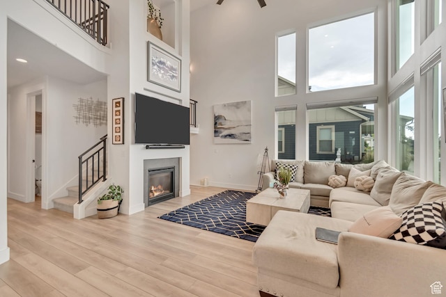 11536 S Allerton Dr, South Jordan, UT 84009 - living area featuring a towering ceiling, a glass covered fireplace, stairs, light wood-type flooring, and a ceiling fan