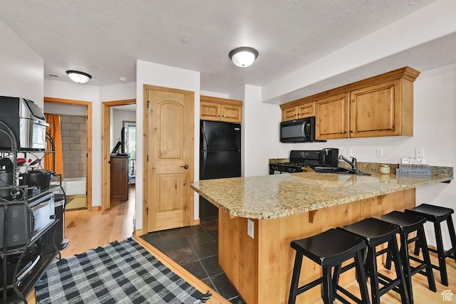 5060 E Lakeview Dr Unit 1109, Eden, UT 84310 - kitchen featuring black appliances, a peninsula, a kitchen breakfast bar, a textured ceiling, and brown cabinets