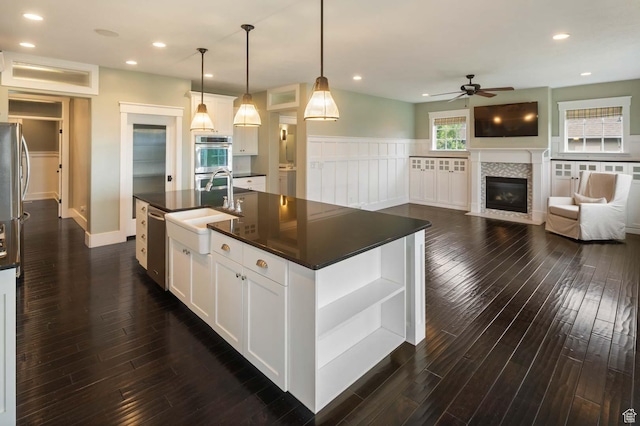 5843 W Wildflower Ln, Highland, UT 84003 - kitchen featuring dark countertops, a ceiling fan, appliances with stainless steel finishes, a tile fireplace, and a center island with sink