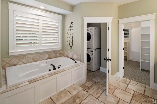 5843 W Wildflower Ln, Highland, UT 84003 - full bathroom featuring stacked washing machine and dryer, a garden tub, stone tile floors, and a walk in closet