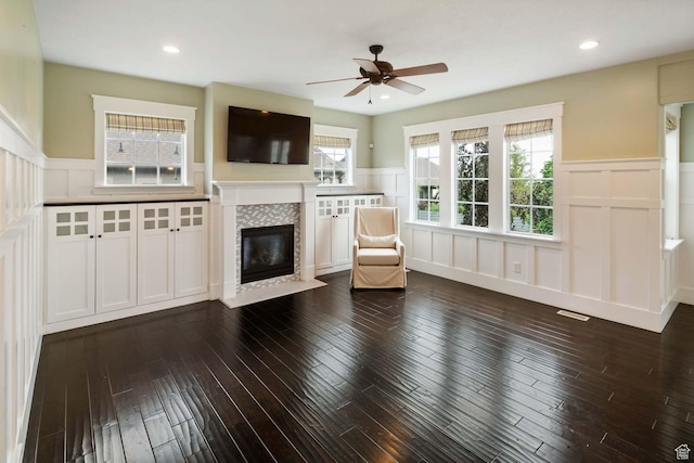 5843 W Wildflower Ln, Highland, UT 84003 - unfurnished living room with a decorative wall, a wainscoted wall, a tiled fireplace, ceiling fan, and dark wood-style flooring