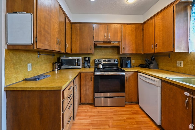 308 W 1050 N, Logan, UT 84321 - kitchen with appliances with stainless steel finishes, under cabinet range hood, light wood finished floors, light countertops, and brown cabinets