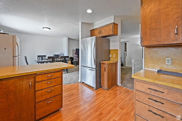 308 W 1050 N, Logan, UT 84321 - kitchen with freestanding refrigerator, light countertops, brown cabinetry, light wood-type flooring, and a textured ceiling