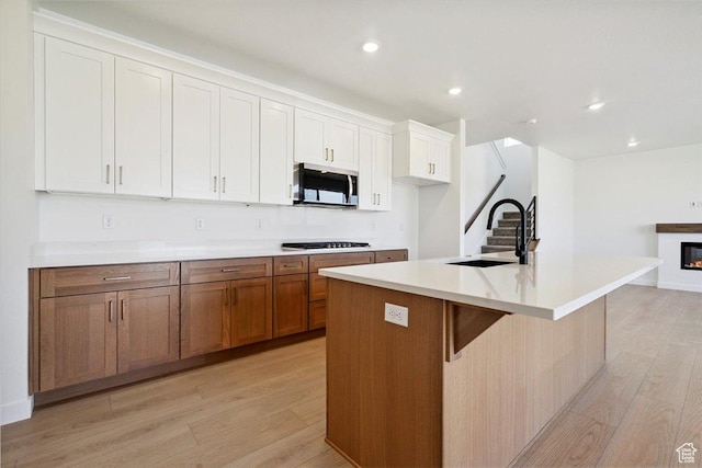 723 N Plainsman Dr Unit 109, Spanish Fork, UT 84660 - kitchen featuring stainless steel microwave, light wood finished floors, gas cooktop, a glass covered fireplace, and white cabinetry