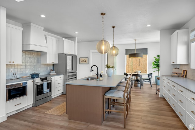6957 W Farnsworth Peak Dr S Unit 314, West Jordan, UT 84081 - kitchen with stainless steel appliances, premium range hood, decorative backsplash, a kitchen island with sink, and recessed lighting