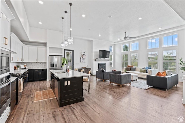 6153 W Poplar View Dr, South Jordan, UT 84009 - kitchen featuring a glass covered fireplace, light wood-style floors, light countertops, ceiling fan, and white cabinetry