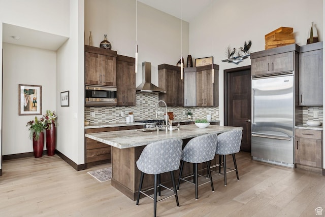 11411 N White Tail Ct, Hideout, UT 84036 - kitchen featuring built in appliances, wall chimney exhaust hood, high vaulted ceiling, light wood finished floors, and tasteful backsplash
