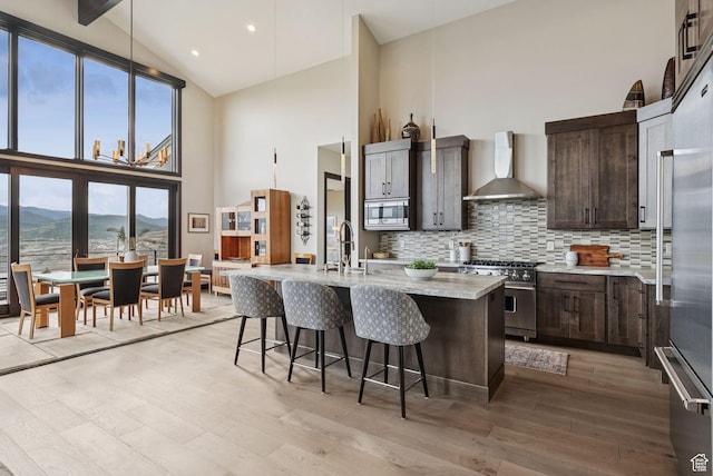 11411 N White Tail Ct, Hideout, UT 84036 - kitchen featuring wall chimney range hood, appliances with stainless steel finishes, high vaulted ceiling, light wood-style flooring, and tasteful backsplash