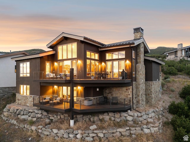 11411 N White Tail Ct, Hideout, UT 84036 - back of property at dusk with stone siding, a balcony, a chimney, a standing seam roof, and a metal roof