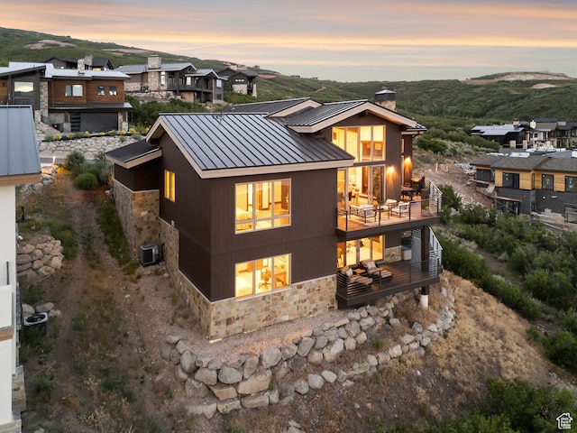11411 N White Tail Ct, Hideout, UT 84036 - back of property at dusk with stone siding, a standing seam roof, a chimney, a metal roof, and a balcony