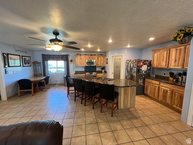 251 N 580 W, Monroe, UT 84754 - kitchen with appliances with stainless steel finishes, light tile patterned floors, a kitchen bar, an island with sink, and a textured ceiling