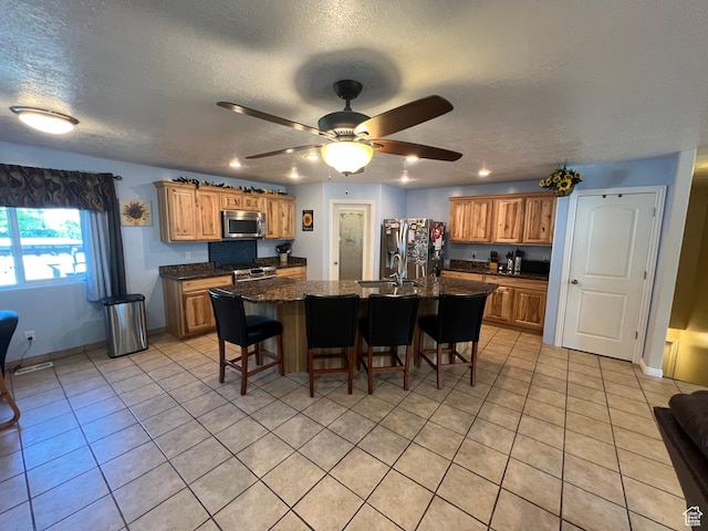 251 N 580 W, Monroe, UT 84754 - kitchen featuring appliances with stainless steel finishes, a breakfast bar area, an island with sink, light tile patterned floors, and a textured ceiling