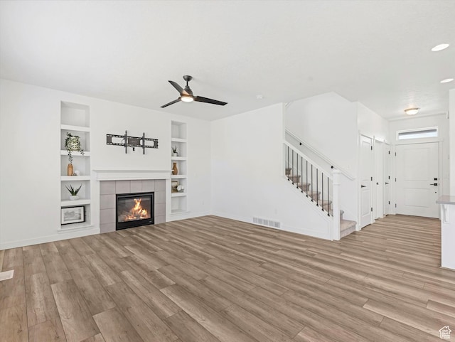 1907 E Brooklyn Cir N, Saratoga Springs, UT 84045 - unfurnished living room with stairs, light wood-style flooring, built in shelves, a ceiling fan, and a fireplace