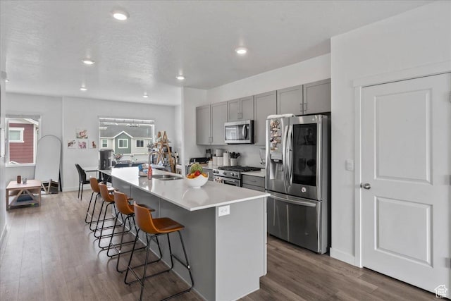 1098 E Vessel Ct, Saratoga Springs, UT 84045 - kitchen featuring appliances with stainless steel finishes, gray cabinets, a kitchen breakfast bar, dark wood-style flooring, and an island with sink