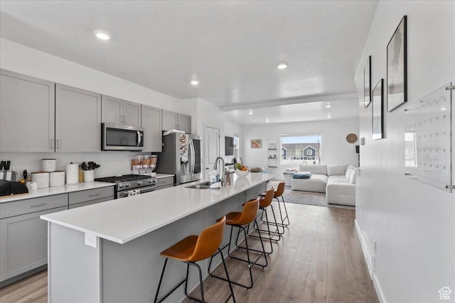 1098 E Vessel Ct, Saratoga Springs, UT 84045 - kitchen with appliances with stainless steel finishes, gray cabinetry, a spacious island, a kitchen bar, and light wood-style floors