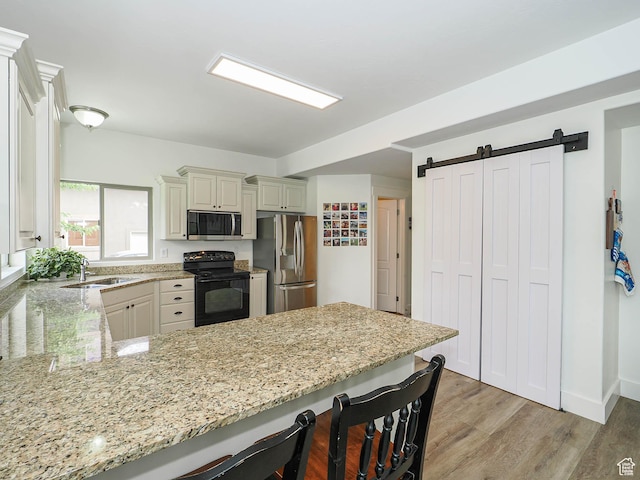 373 N Willow Haven Ave, Lehi, UT 84043 - kitchen featuring appliances with stainless steel finishes, a kitchen bar, a barn door, a peninsula, and light stone counters