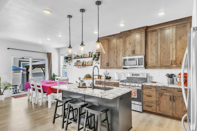 2456 W Maple St, Mapleton, UT 84664 - kitchen with stainless steel appliances, backsplash, light wood-style floors, a kitchen island with sink, and light stone countertops