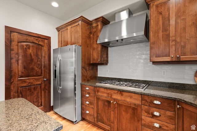 4048 W Ivy Ave, Mountain Green, UT 84050 - kitchen featuring appliances with stainless steel finishes, wall chimney exhaust hood, light wood-type flooring, dark stone counters, and backsplash