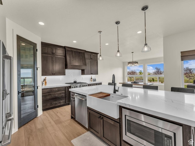 943 Hart Loop, Francis, UT 84036 - kitchen with premium range hood, stainless steel appliances, dark brown cabinetry, light wood-type flooring, and tasteful backsplash