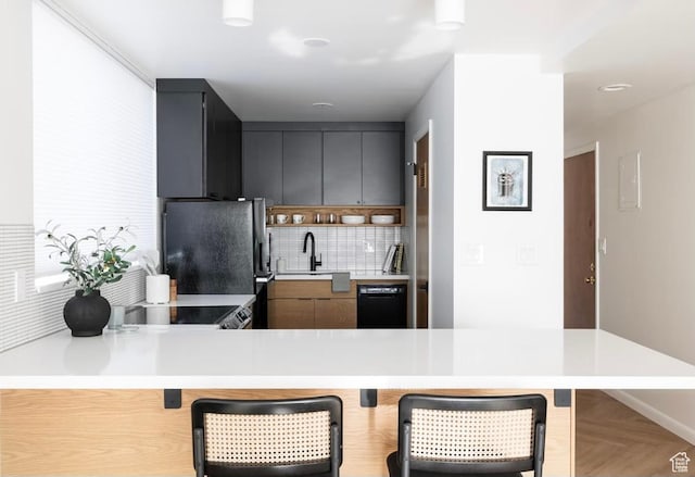 673 E 6th Ave, Salt Lake City, UT 84103 - kitchen with black appliances, a breakfast bar area, decorative backsplash, light countertops, and a peninsula
