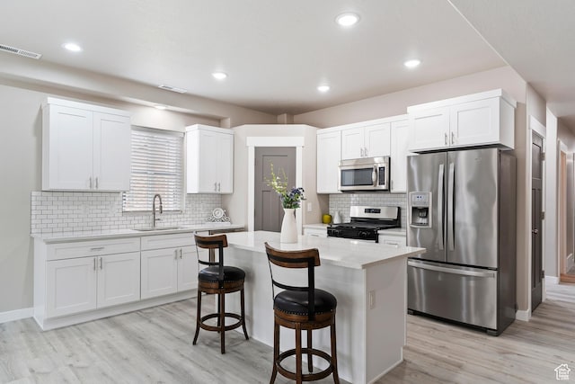 2835 Lincoln Ave, Ogden, UT 84401 - kitchen with stainless steel appliances, a kitchen bar, light wood-type flooring, white cabinets, and a kitchen island