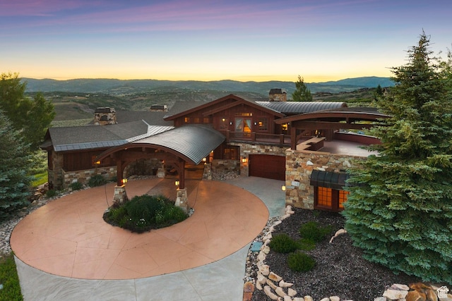 7881 N W Hills Trl, Park City, UT 84098 - view of front of property featuring stone siding, a chimney, curved driveway, a mountain view, and a garage