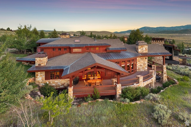 7881 N W Hills Trl, Park City, UT 84098 - back of property at dusk with a chimney, stone siding, a deck with mountain view, and a metal roof