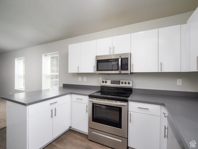 1141 E 1320 S Unit A401, Provo, UT 84606 - kitchen featuring appliances with stainless steel finishes, a peninsula, white cabinetry, wood finished floors, and dark countertops