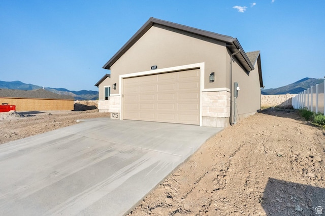 1182 N Berra Blvd, Tooele, UT 84074 - view of side of property with a mountain view, driveway, stone siding, stucco siding, and an attached garage