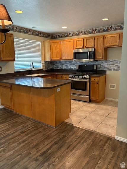 1579 W 2050 N, Clinton, UT 84015 - kitchen with appliances with stainless steel finishes, dark countertops, a peninsula, brown cabinetry, and decorative backsplash