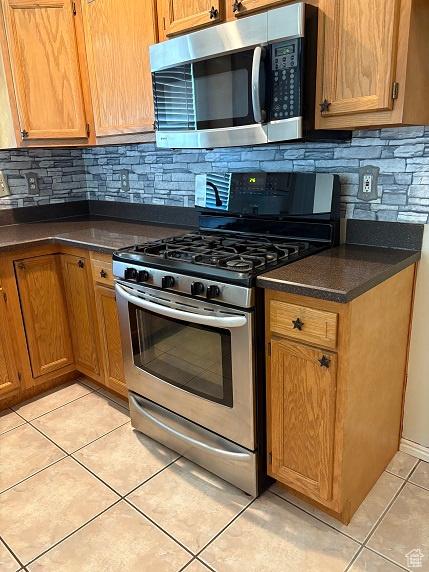 1579 W 2050 N, Clinton, UT 84015 - kitchen featuring stainless steel appliances, light tile patterned floors, dark countertops, decorative backsplash, and brown cabinets