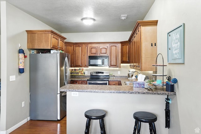 1492 N 565 W Unit 101, Logan, UT 84341 - kitchen featuring stainless steel appliances, a peninsula, a kitchen breakfast bar, dark wood-style flooring, and a textured ceiling