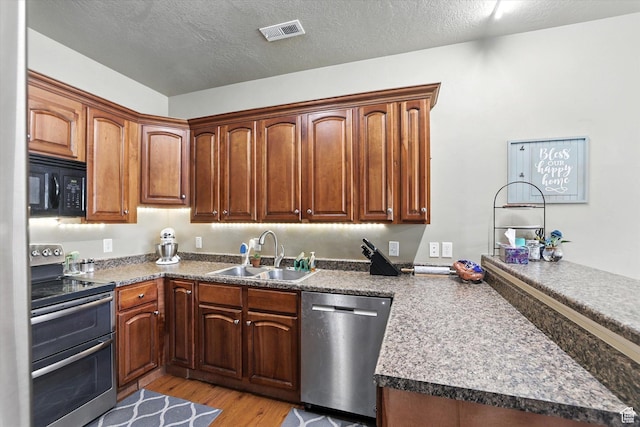 1492 N 565 W Unit 101, Logan, UT 84341 - kitchen featuring stainless steel appliances, a peninsula, light wood-style floors, a textured ceiling, and brown cabinets