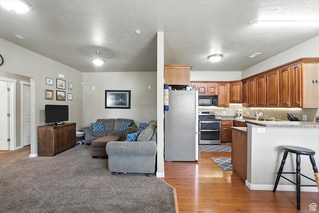 1492 N 565 W Unit 101, Logan, UT 84341 - kitchen with appliances with stainless steel finishes, a peninsula, open floor plan, a breakfast bar, and brown cabinets