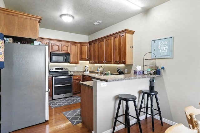 1492 N 565 W Unit 101, Logan, UT 84341 - kitchen featuring appliances with stainless steel finishes, a peninsula, dark wood-type flooring, a breakfast bar area, and a textured ceiling