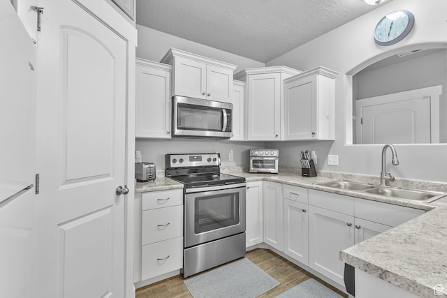 217 W Ridge Rd, Saratoga Springs, UT 84045 - kitchen with stainless steel appliances, light wood-type flooring, white cabinetry, light countertops, and arched walkways