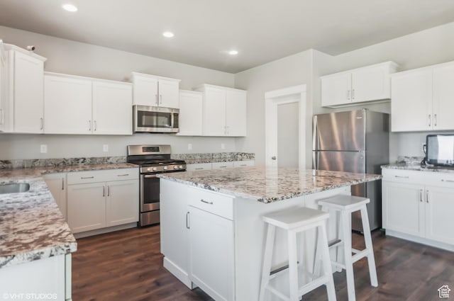 2086 W White Pine Dr S, Layton, UT 84041 - kitchen featuring appliances with stainless steel finishes, a center island, dark wood finished floors, a kitchen breakfast bar, and light stone countertops